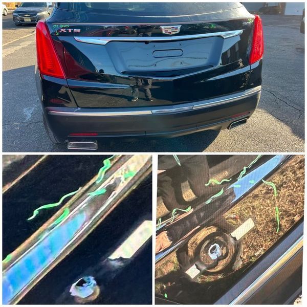 Black Cadillac XT5's rear bumper with damaged chrome trim and green tape.