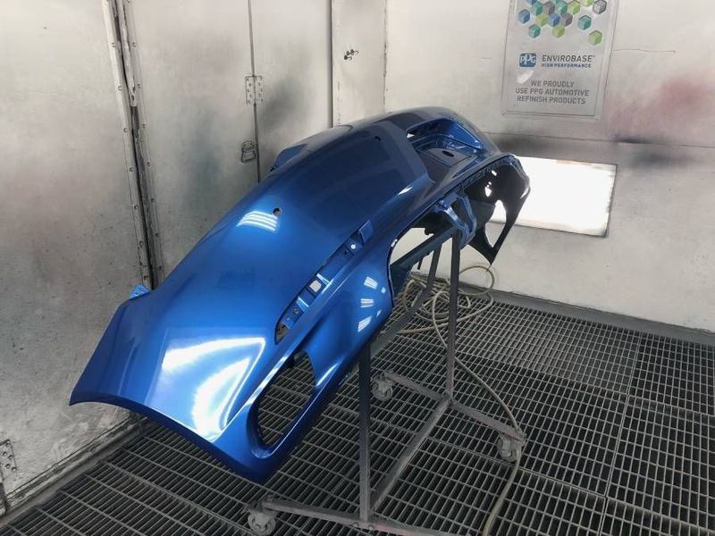 Blue car bumper freshly painted, sitting on a stand in a paint booth.