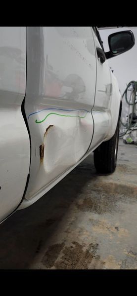White pickup truck side with a dent and rust near the bottom.
