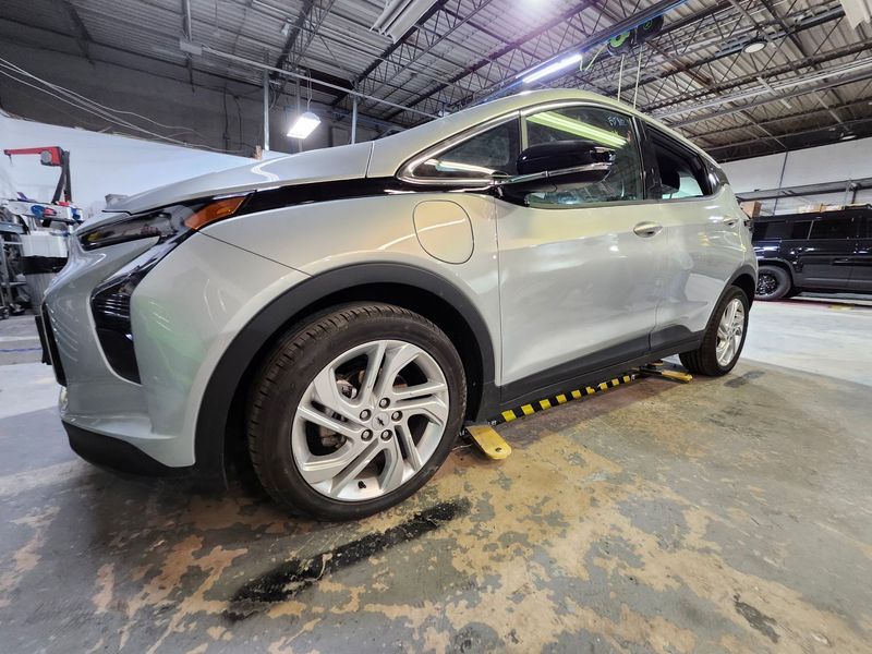Silver electric car with front-end damage on a garage floor.