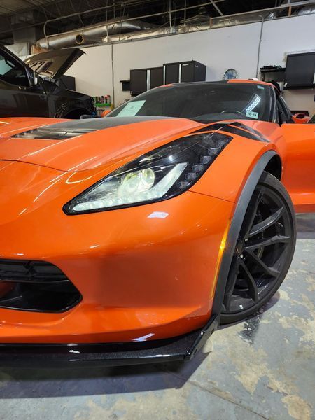 Orange sports car with black accents and wheels, open door, parked indoors.