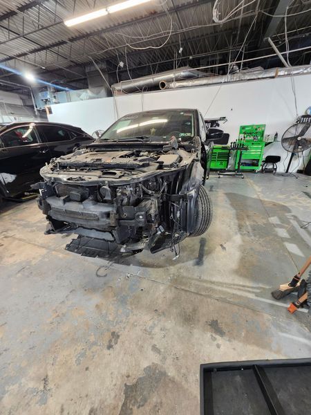 Car in auto repair shop, front end disassembled, black paint, gray concrete floor.