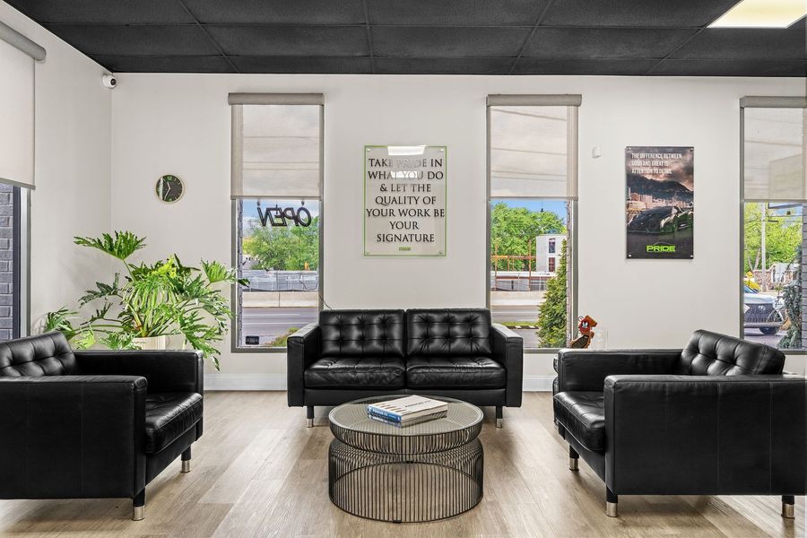 Waiting area with black leather furniture, round coffee table, and large windows. Includes plant and art.