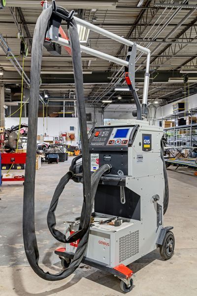 Gray welding machine with hoses and controls on wheels in a workshop setting.