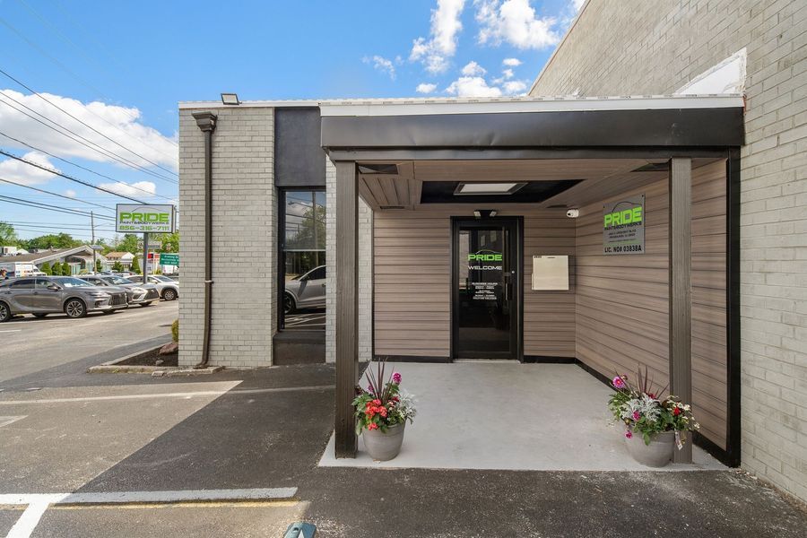 Exterior of a business with a covered entrance, gray and beige facade, and potted flowers.