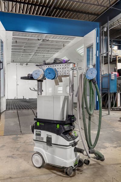 White and black shop vacuum with attached accessories, hose, and sanding pads, in a body shop.