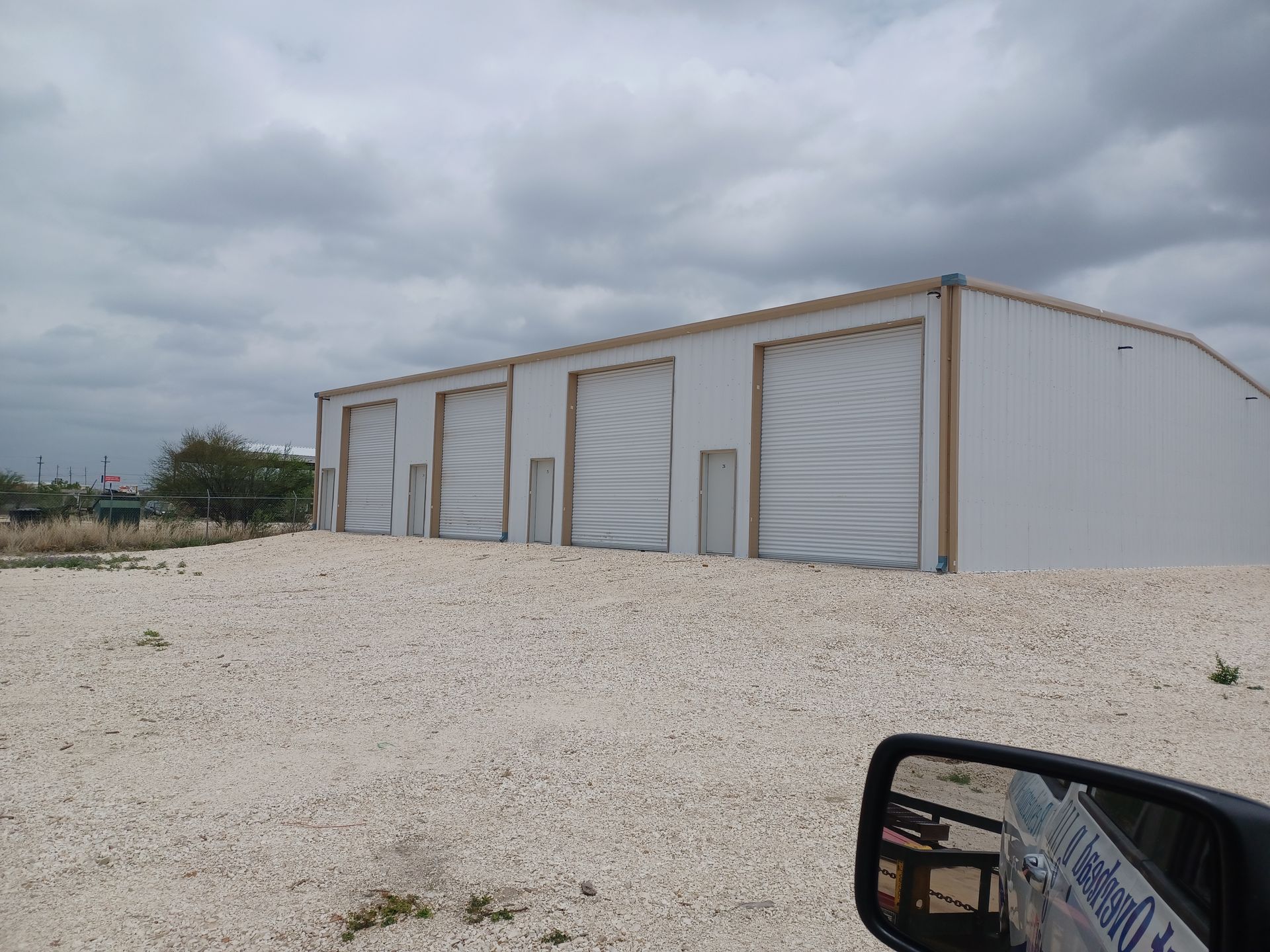 White metal storage building with several garage doors, set on a gravel lot under a cloudy sky.