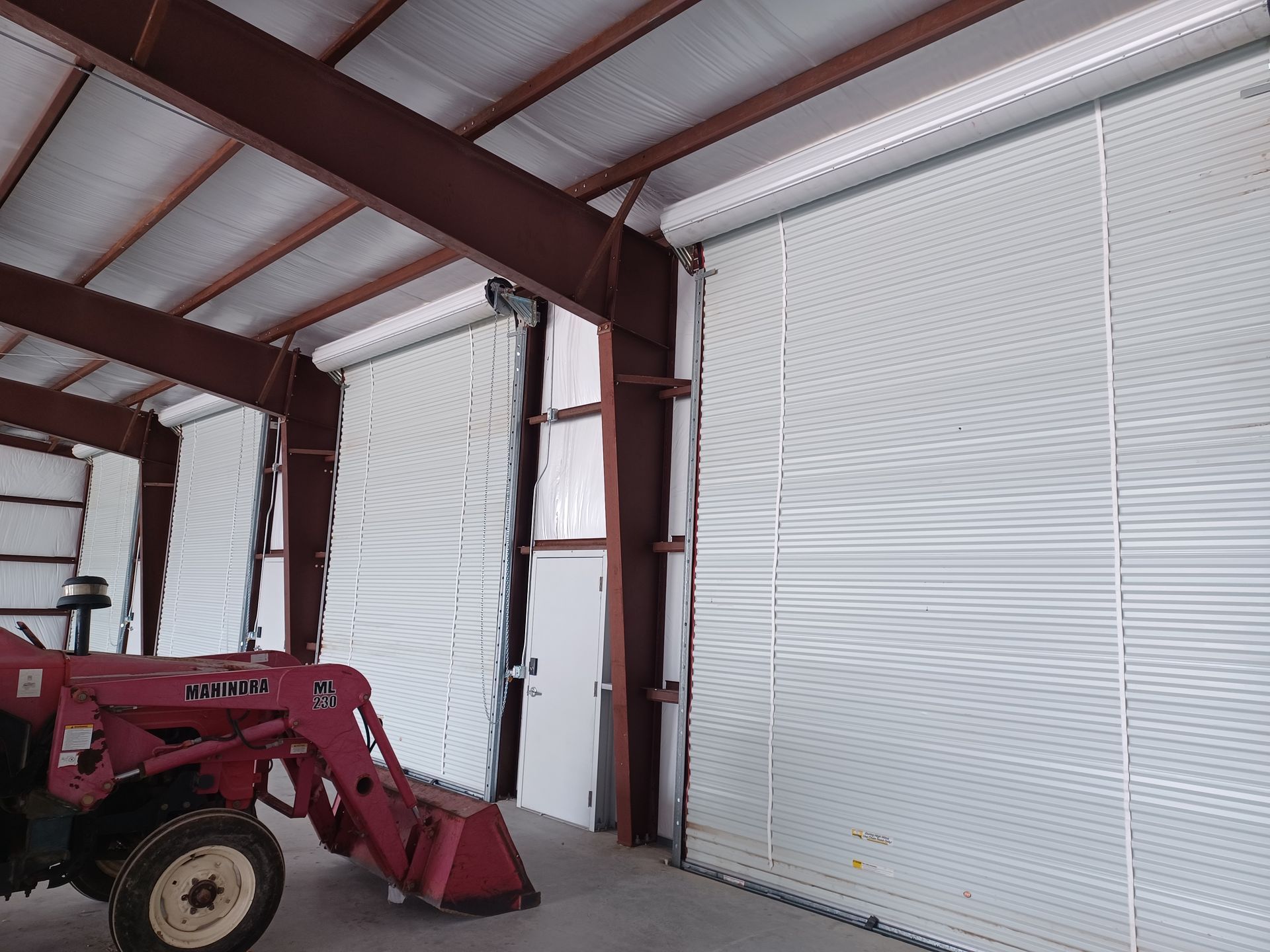 Red tractor inside a metal building with large, white roll-up doors.