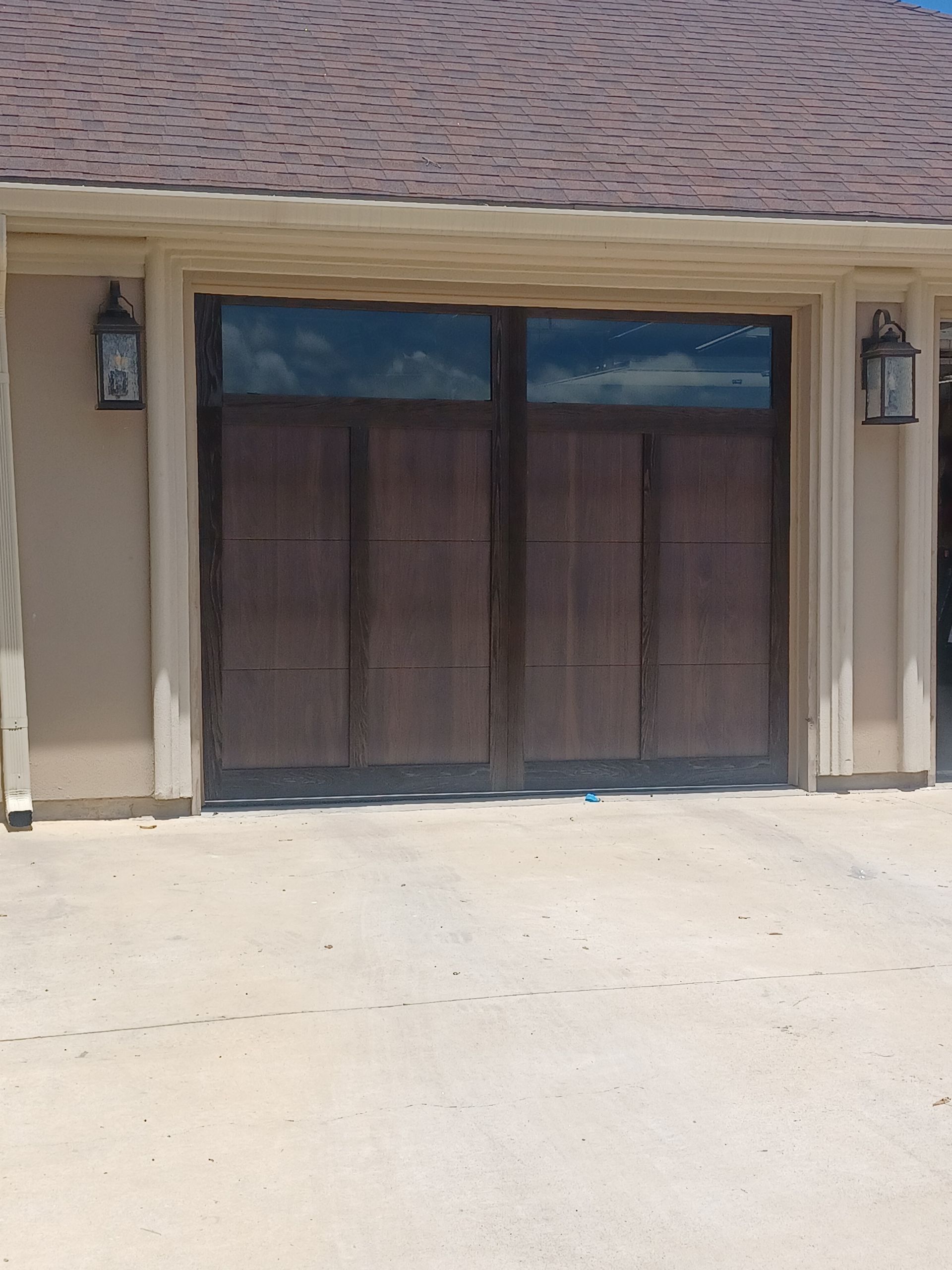 Dark wood garage door with glass, tan exterior, and roof with cloud reflections.