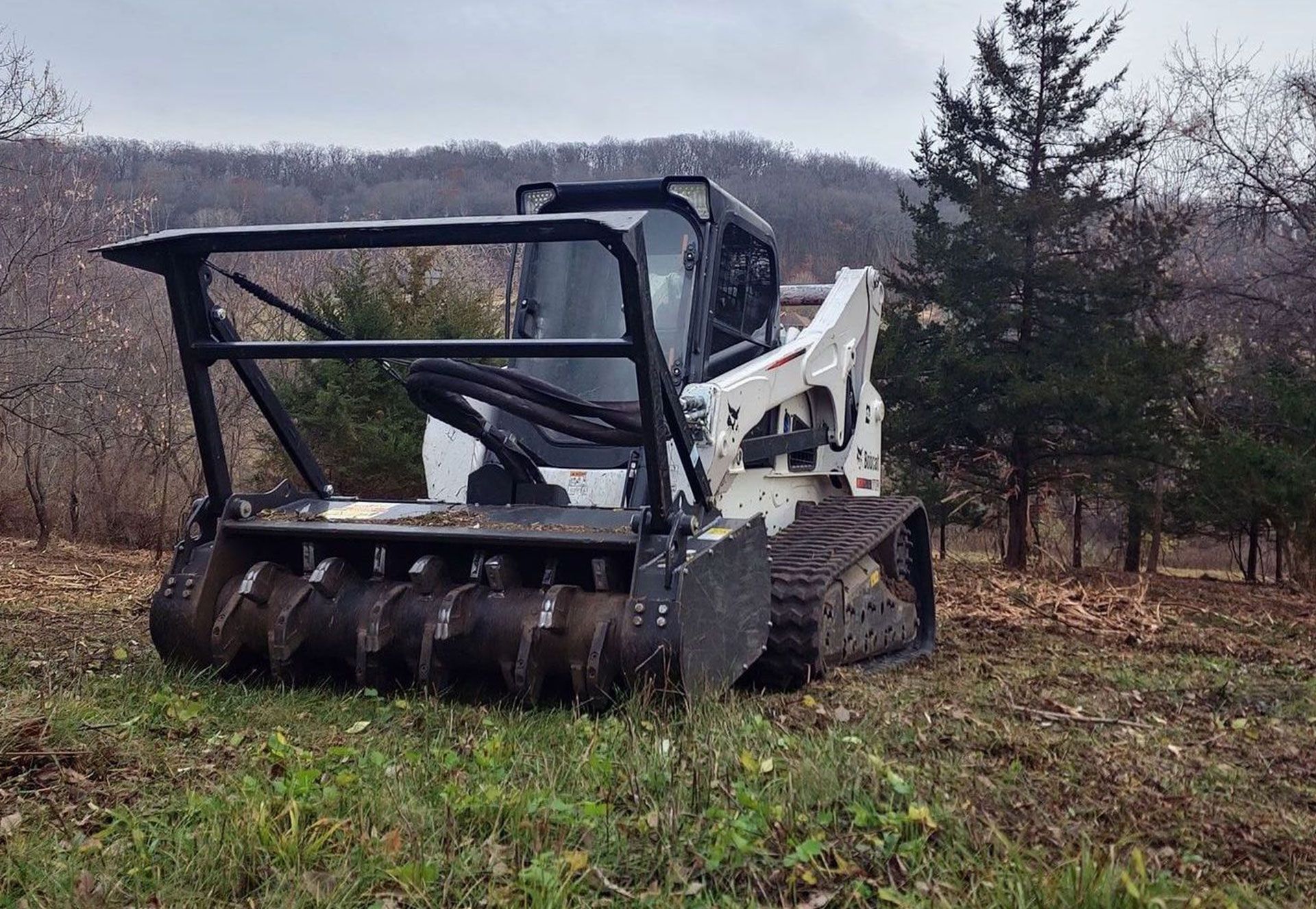 A bulldozer is cutting grass in a field with trees in the background.