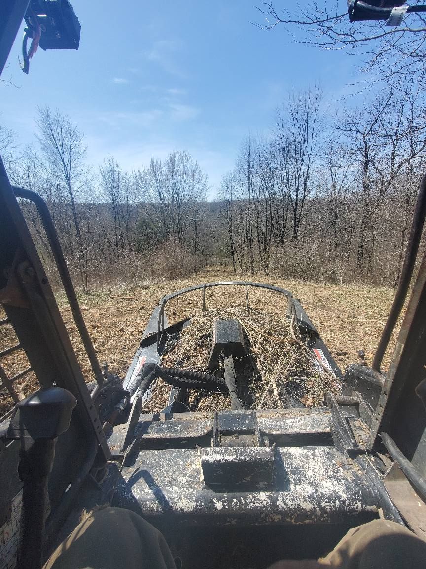 A person is driving a tractor through a field with trees in the background.