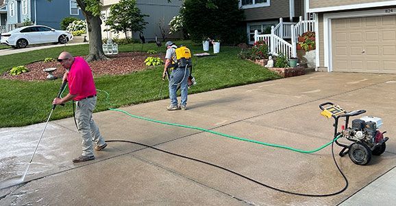 Two men are cleaning a driveway with a pressure washer.