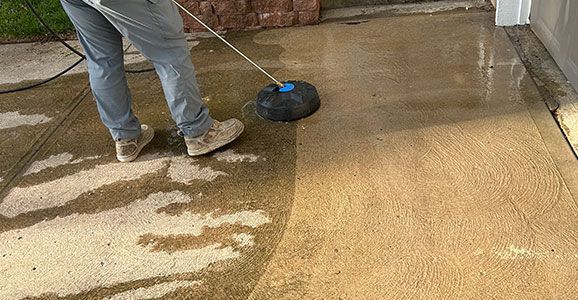 A person is cleaning a concrete driveway with a pressure washer.