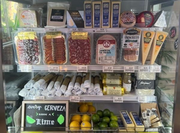 Store display case with assorted packaged snacks, cigarettes, and drinks on glass shelves.