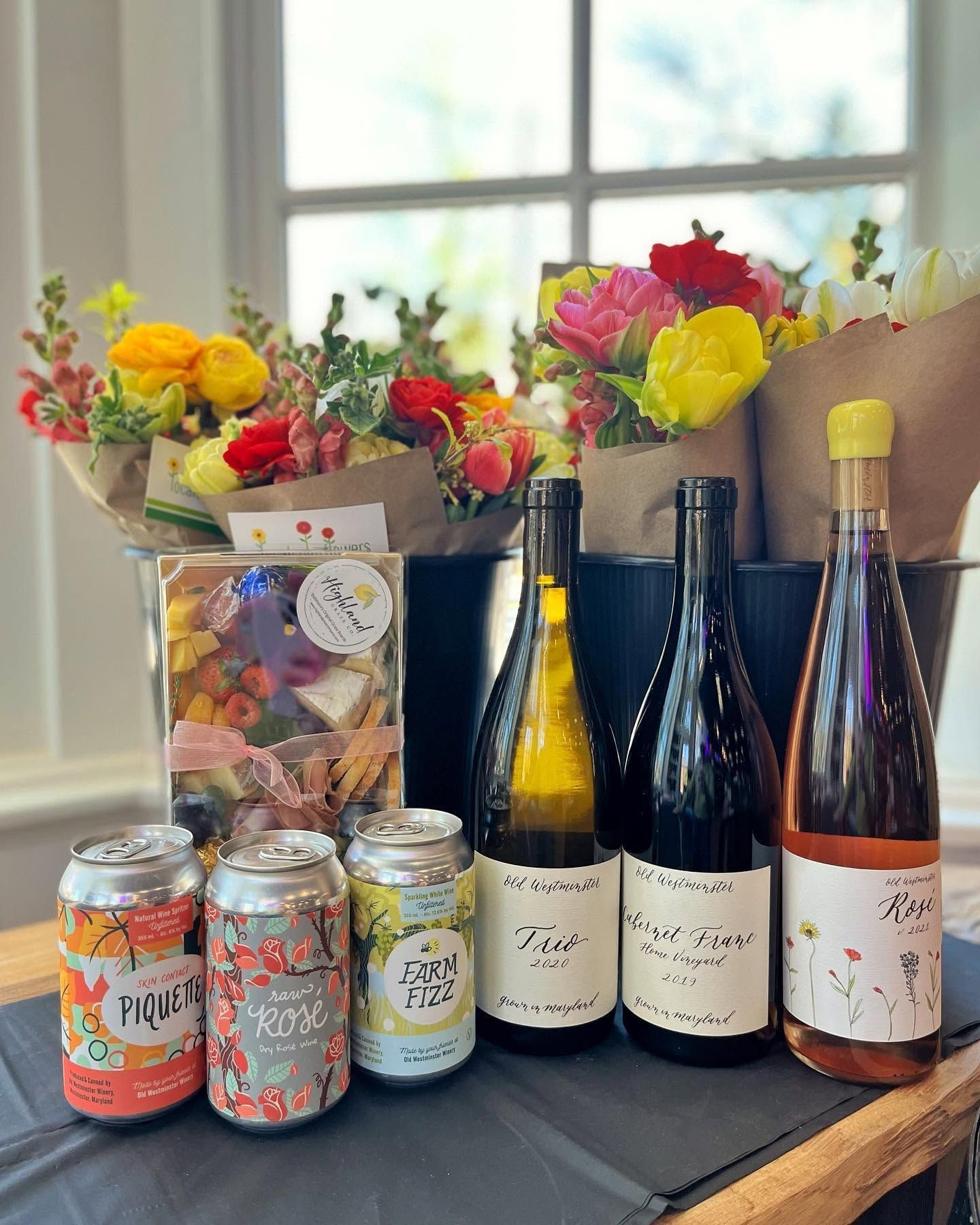 Colorful flowers, wine bottles, and cans arranged on a table by a bright window