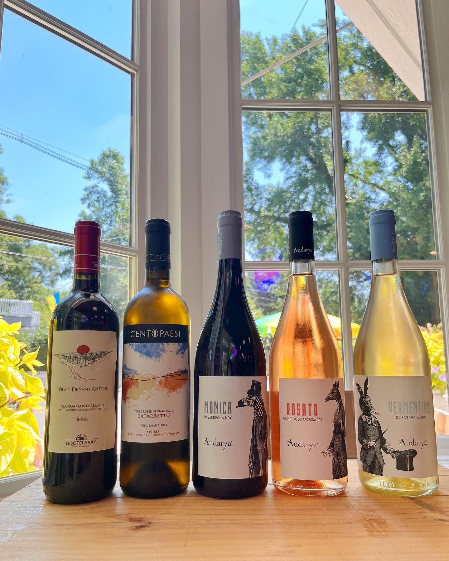 Five wine bottles on a windowsill with a bright outdoor view behind them