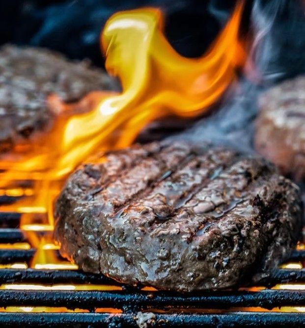 Grilled hamburger patty with flames rising on a barbecue grate
