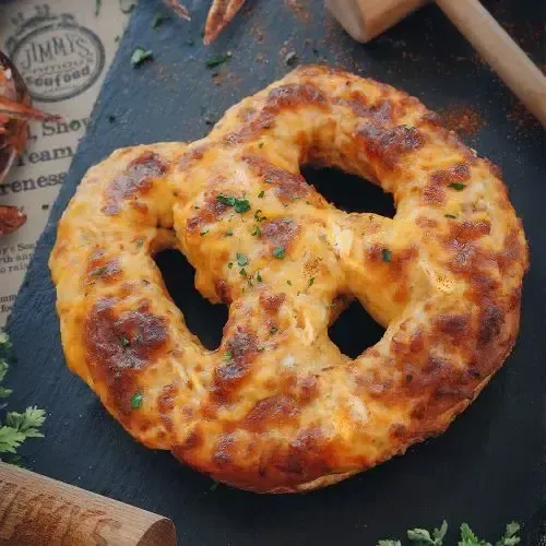 Baked pretzel with melted cheese on a dark slate board, garnished with herbs.