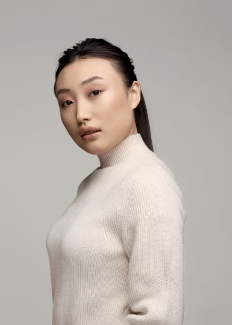 Portrait of a person in a cream turtleneck sweater against a plain gray background