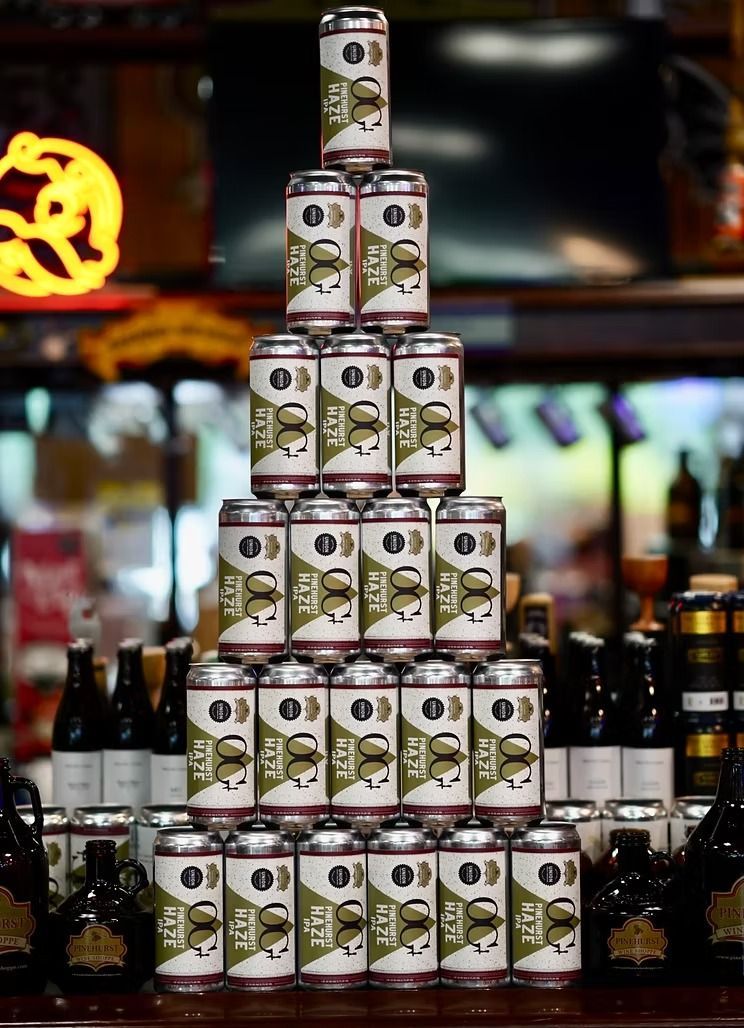 Stacked beer cans arranged in a pyramid on a bar counter, with bottles blurred in the background
