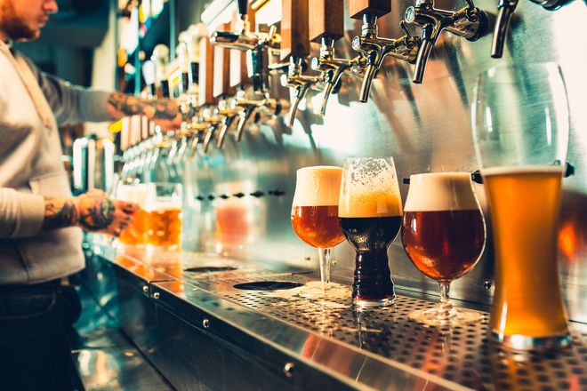 Beer taps pouring assorted craft beers at a bar counter, with a person serving in the background