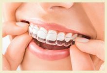 Person smiling while adjusting clear braces on their teeth.
