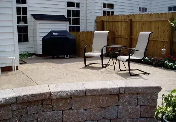 Patio with two chairs, small table, and a grill. Stone wall in the foreground.