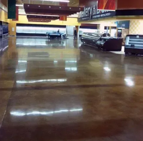 Polished concrete floor in a nearly empty supermarket. Display cases, and Bakery & Deli sign visible.