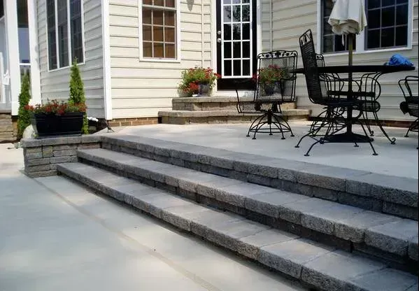 Covered porch of a building with a concrete floor. Columns have stone bases. Asphalt parking lot visible.