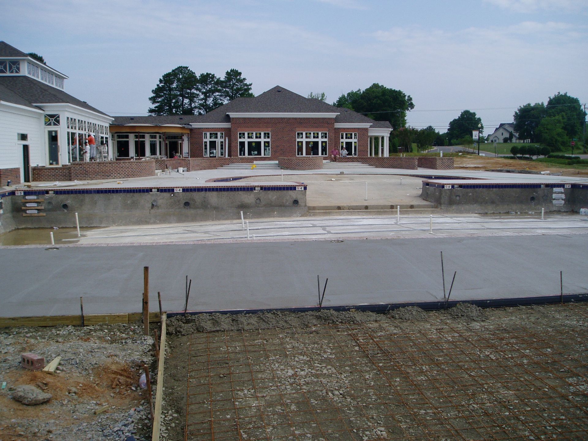 Construction site: unfinished swimming pool, brick building in background.