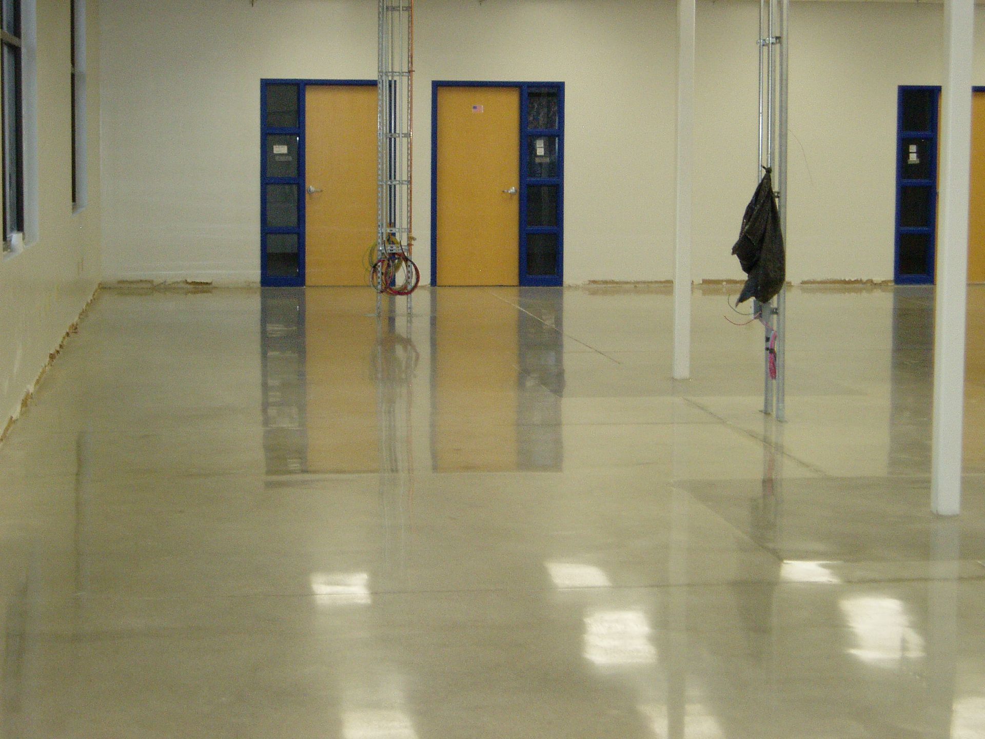 Polished concrete floor in a mostly empty room with beige doors and vertical support poles.
