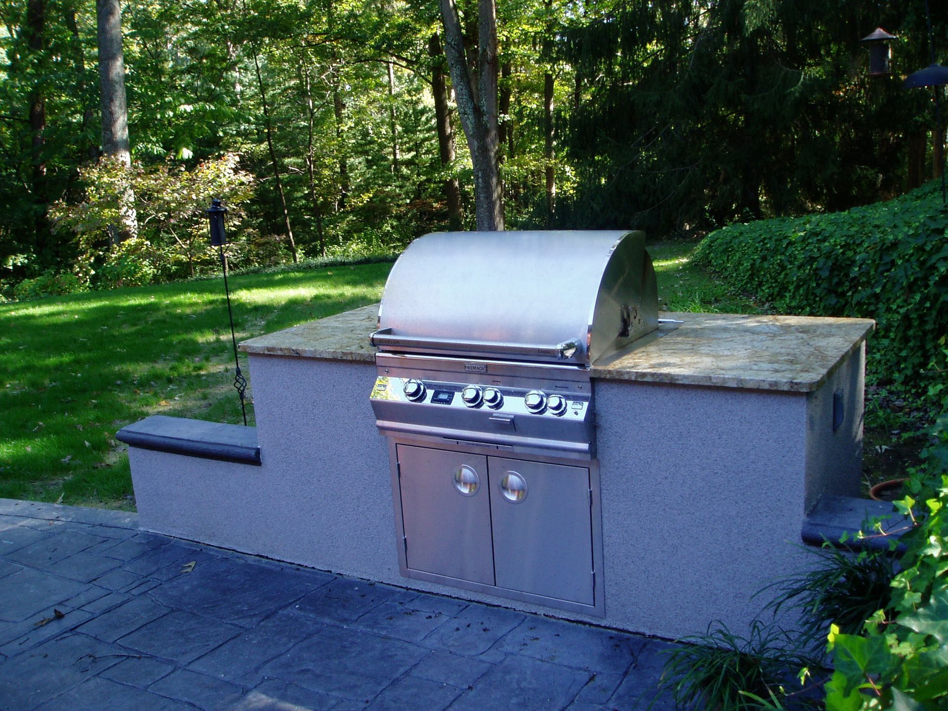 Built-in outdoor grill with stainless steel features on a concrete structure with stone countertop, backyard setting.