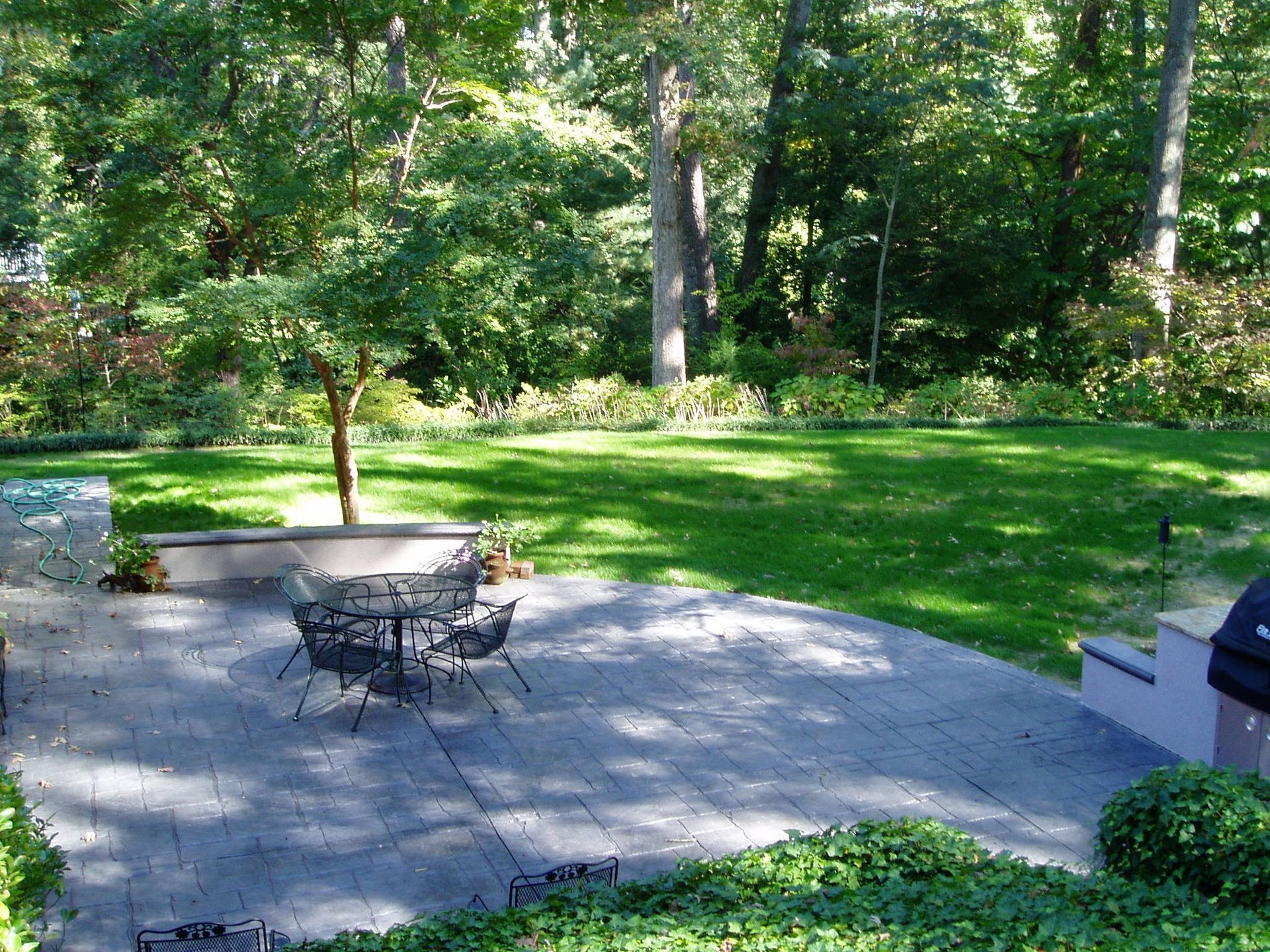 Patio with table and chairs, overlooking a grassy yard with trees in the background.