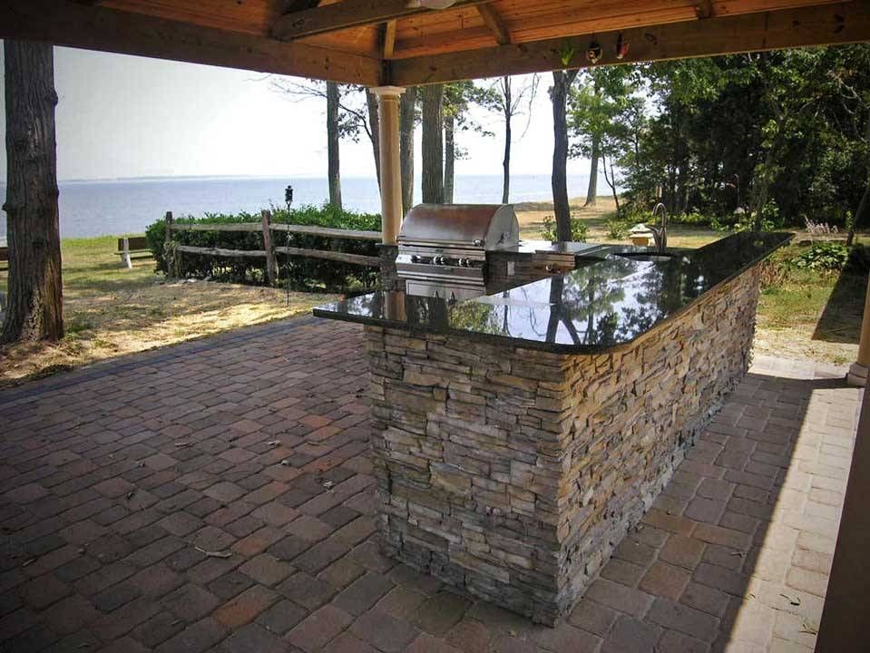 Outdoor kitchen with stone facade and black countertop, overlooking a body of water.