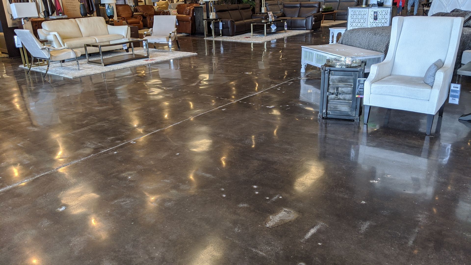 Polished concrete floor in a furniture store, reflecting overhead lights, with couches and chairs displayed.