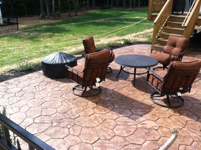 Patio with four brown swivel chairs, a round table, fire pit, and stairs, on stamped concrete.