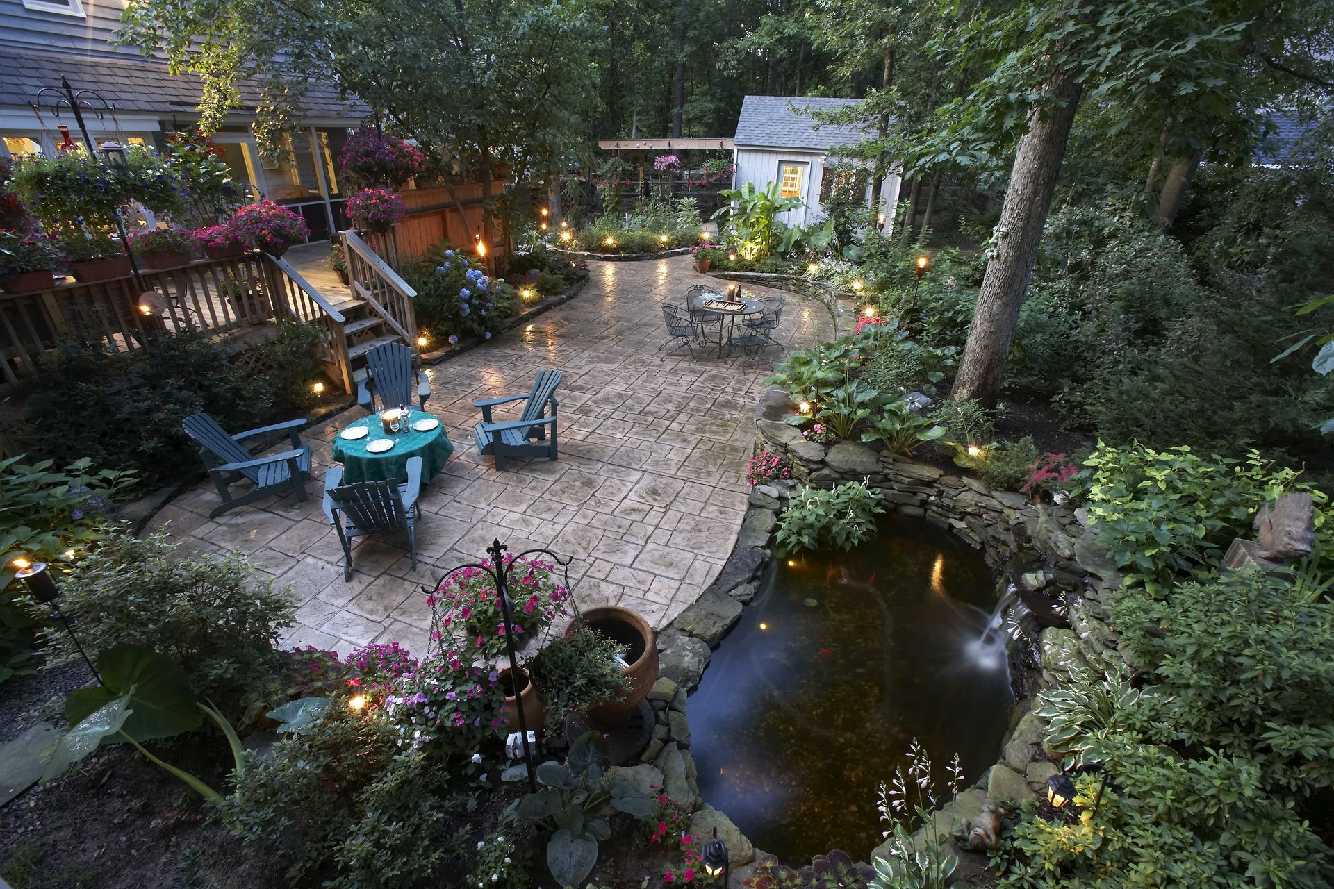 Brick patio with tables, chairs, and pond surrounded by plants and garden lights.