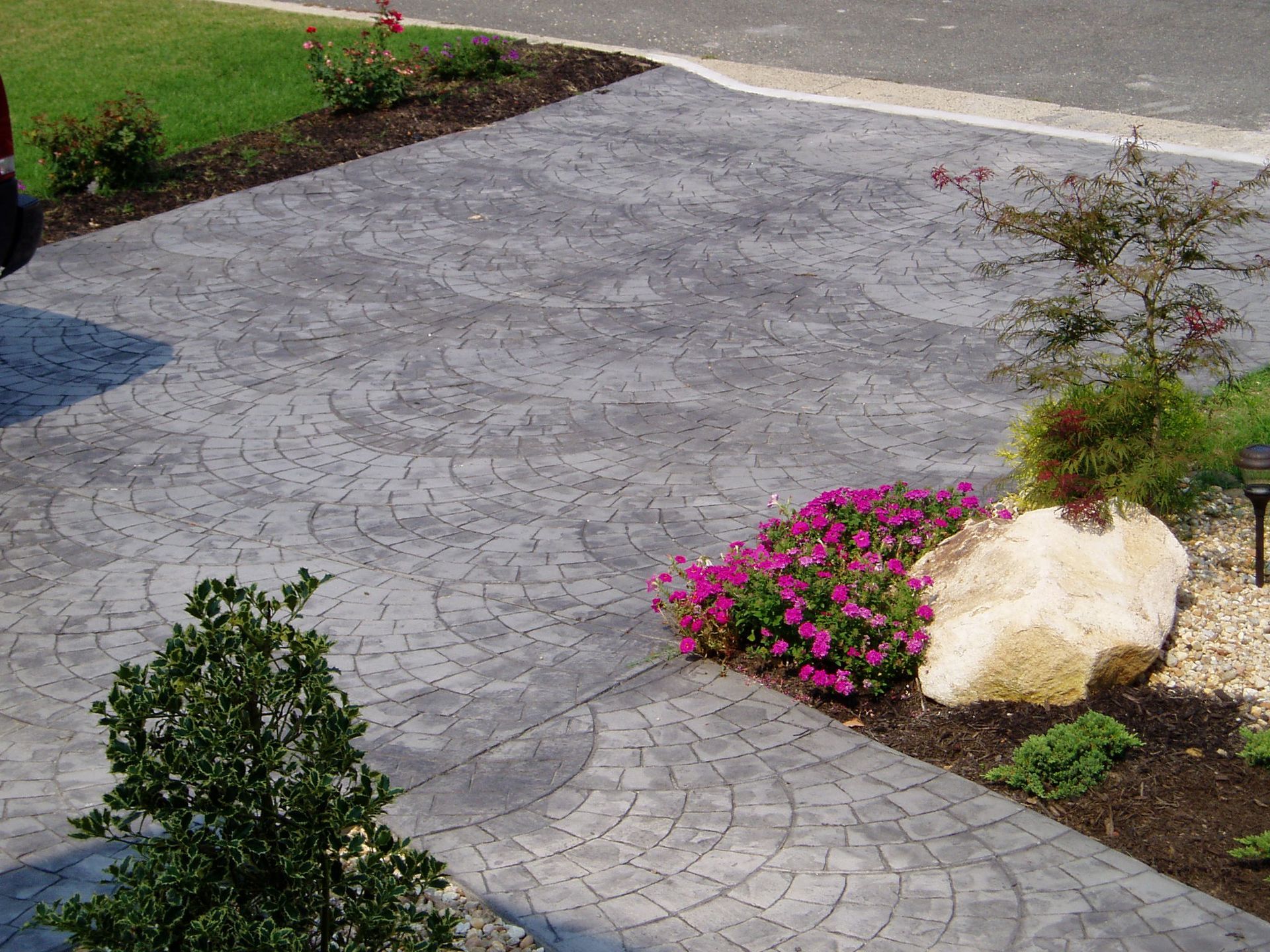 Stamped concrete driveway with circular pattern, bordered by landscaping and plants.