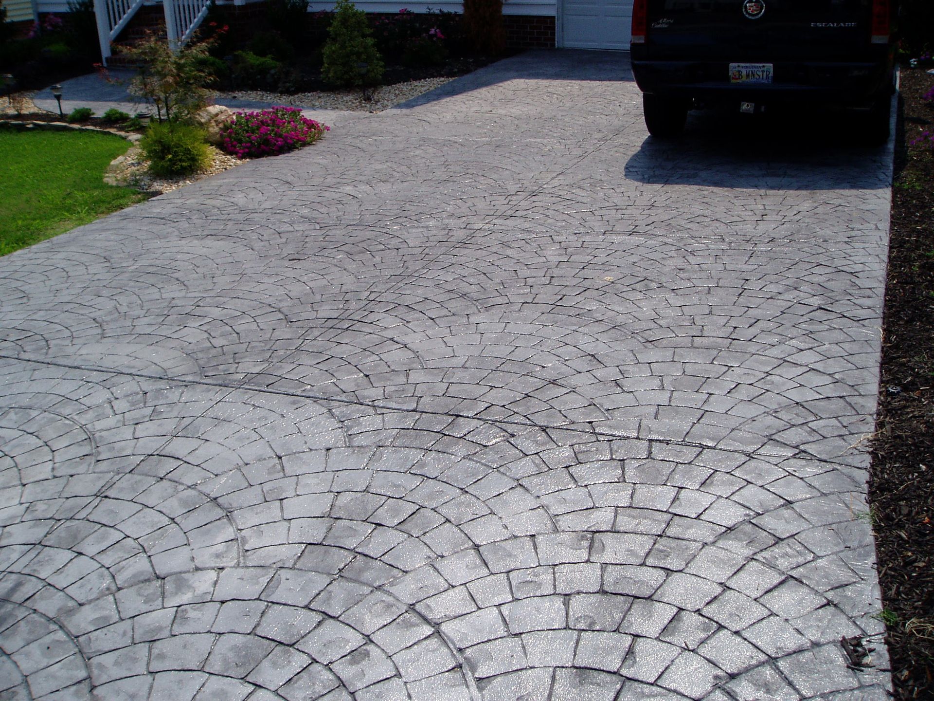 Gray, patterned concrete driveway with a black car parked at the end.