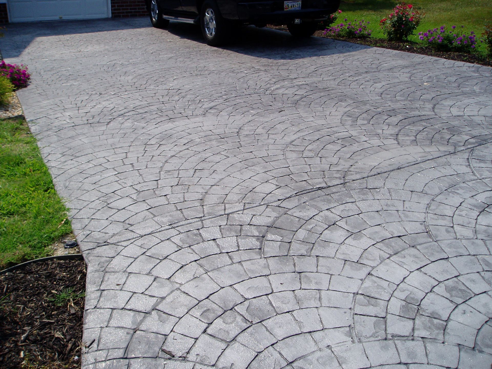 Concrete driveway with circular brick pattern; a black vehicle is parked in it.