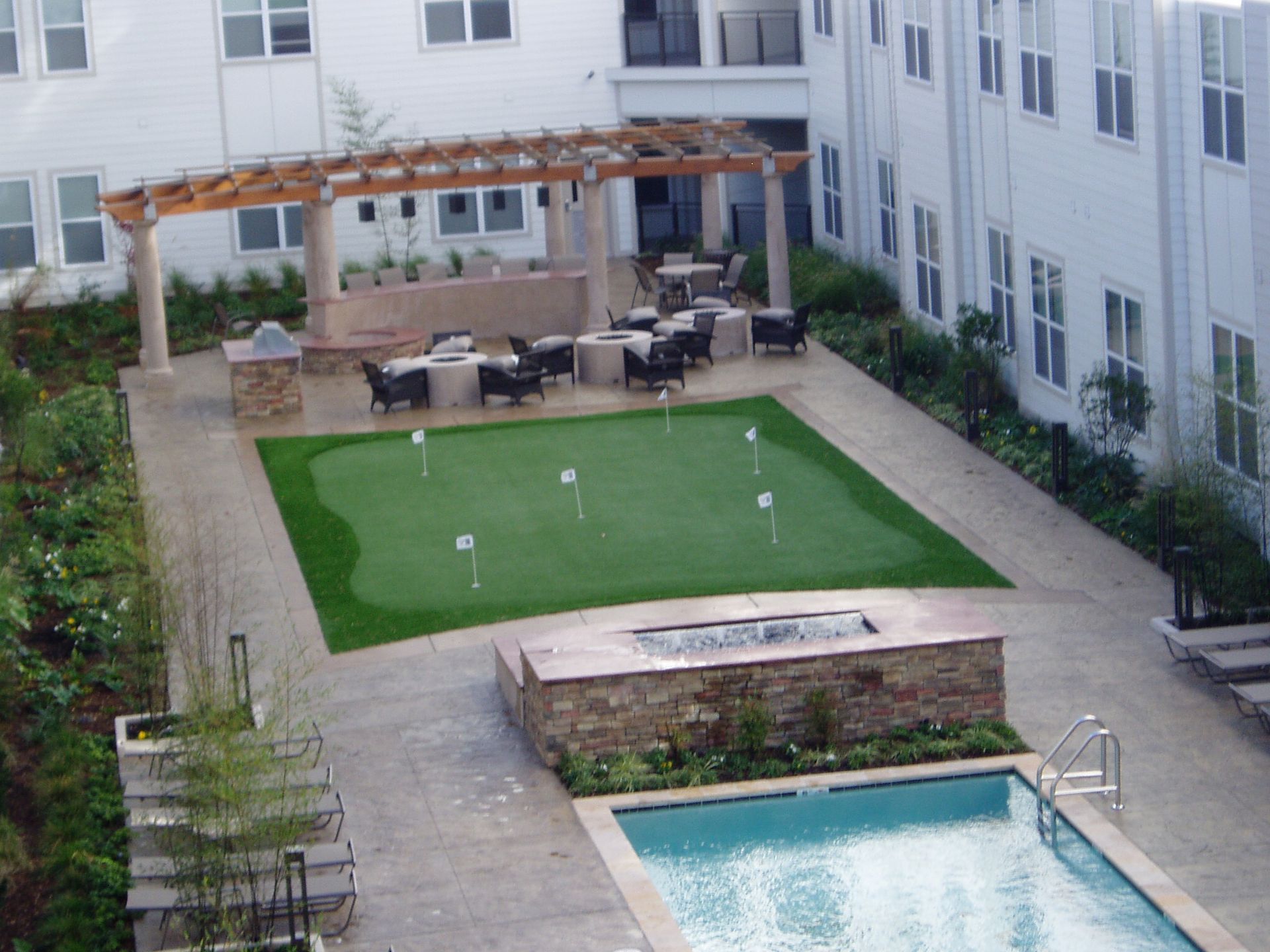 Outdoor space with putting green, seating area, pool, and fire pit in a modern building courtyard.