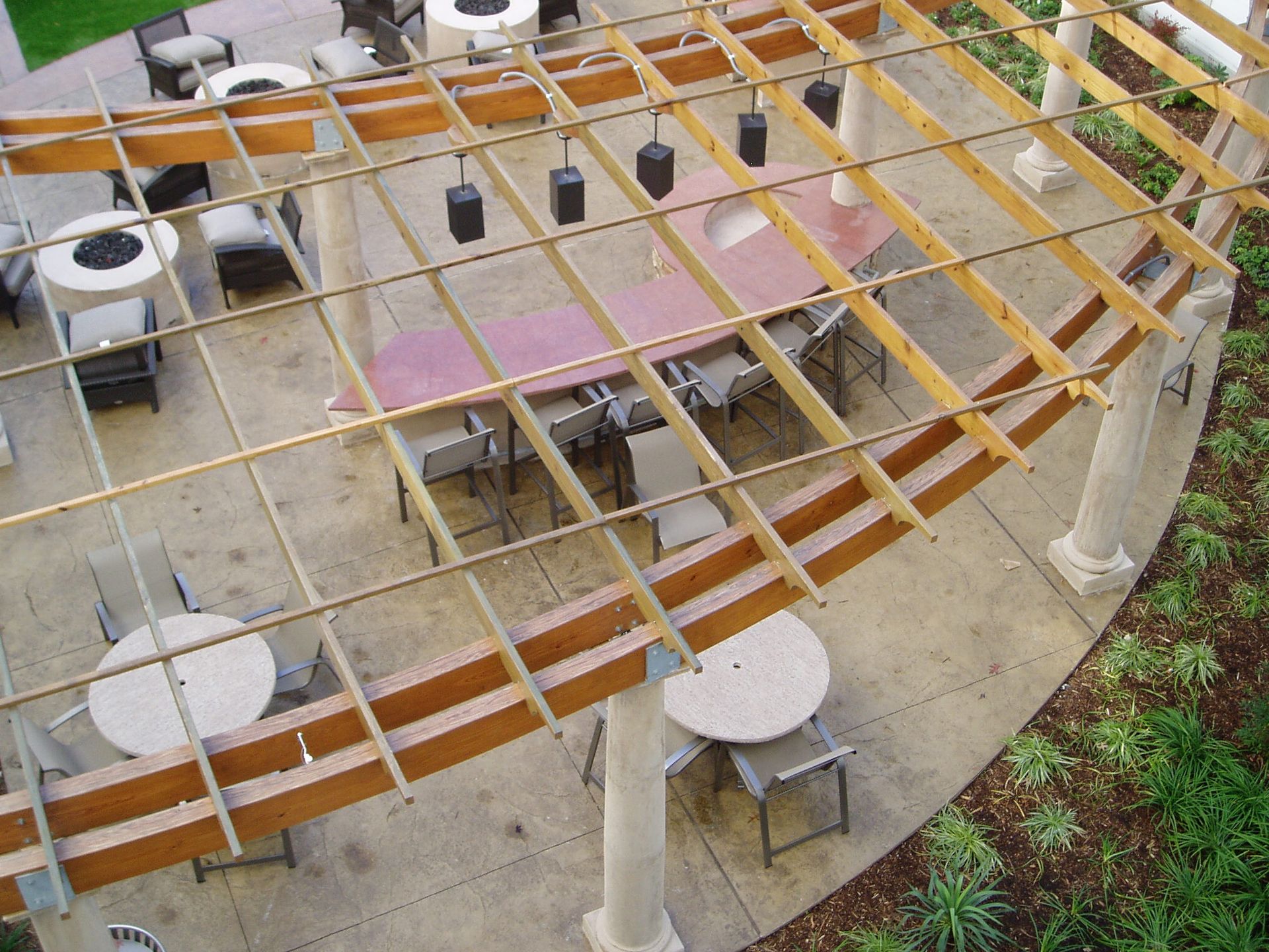 Outdoor patio with tables, chairs, and a wooden pergola overhead. Concrete columns support the structure.