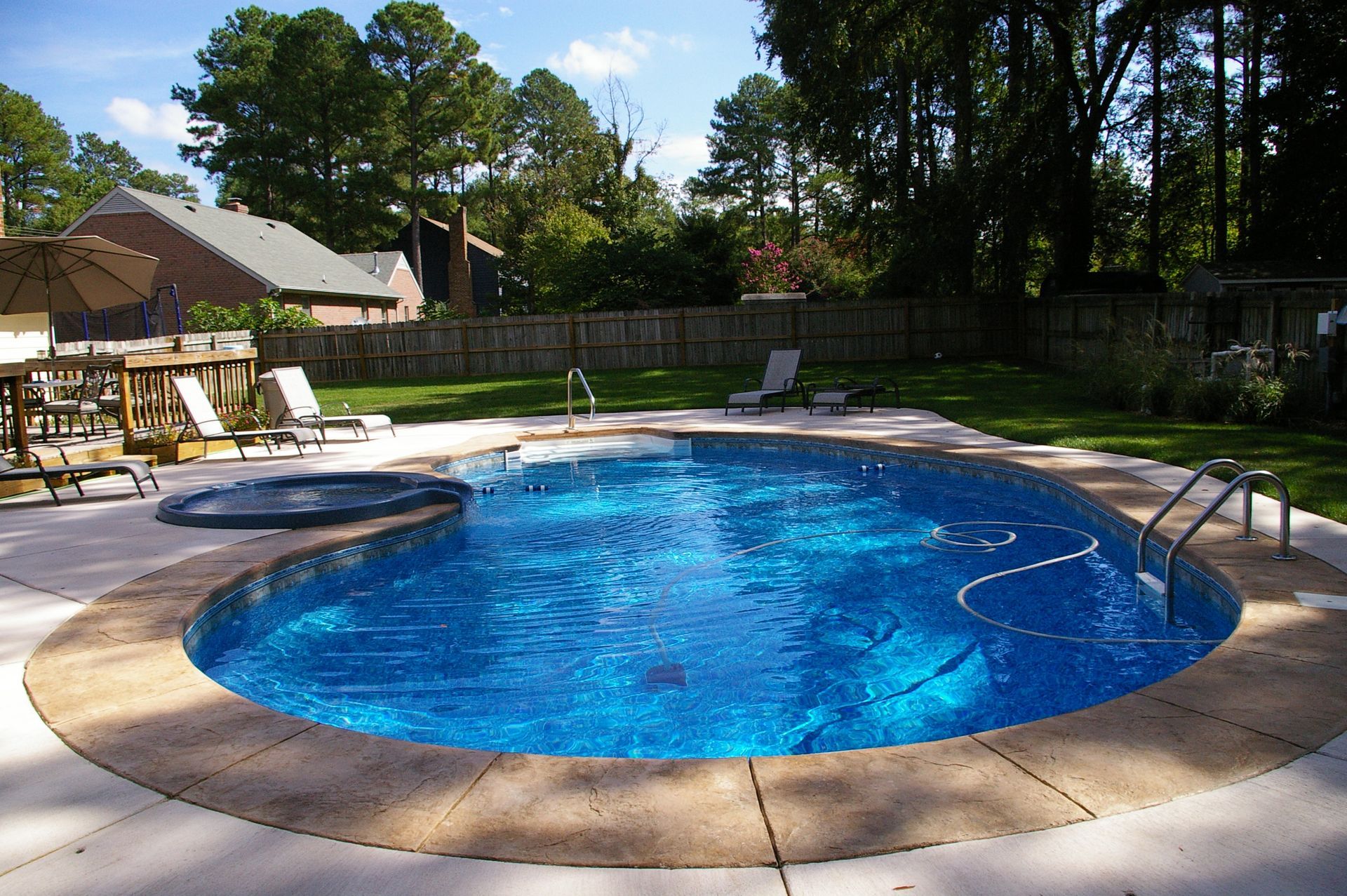 Backyard pool with surrounding concrete, lounge chairs, and wooden deck.