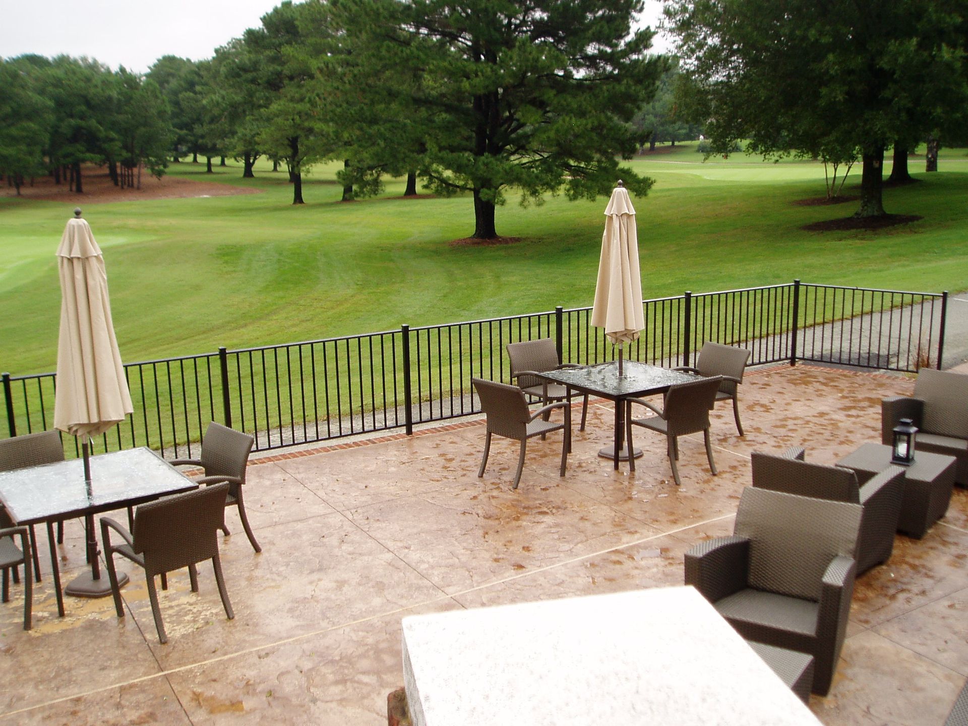 Outdoor patio with tables, chairs, and umbrellas overlooking a golf course with green grass and trees.