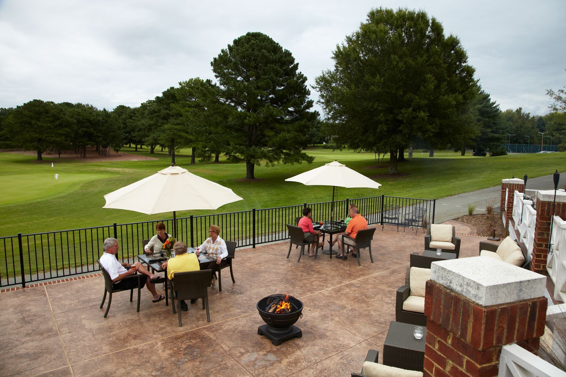 Patio with tables, umbrellas, and people overlooking a golf course.