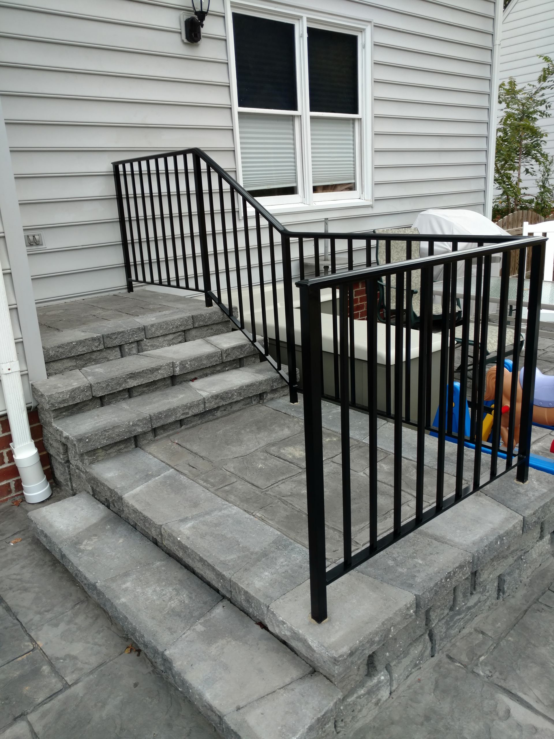 Black metal railing on gray stone steps leading to a house with white siding.