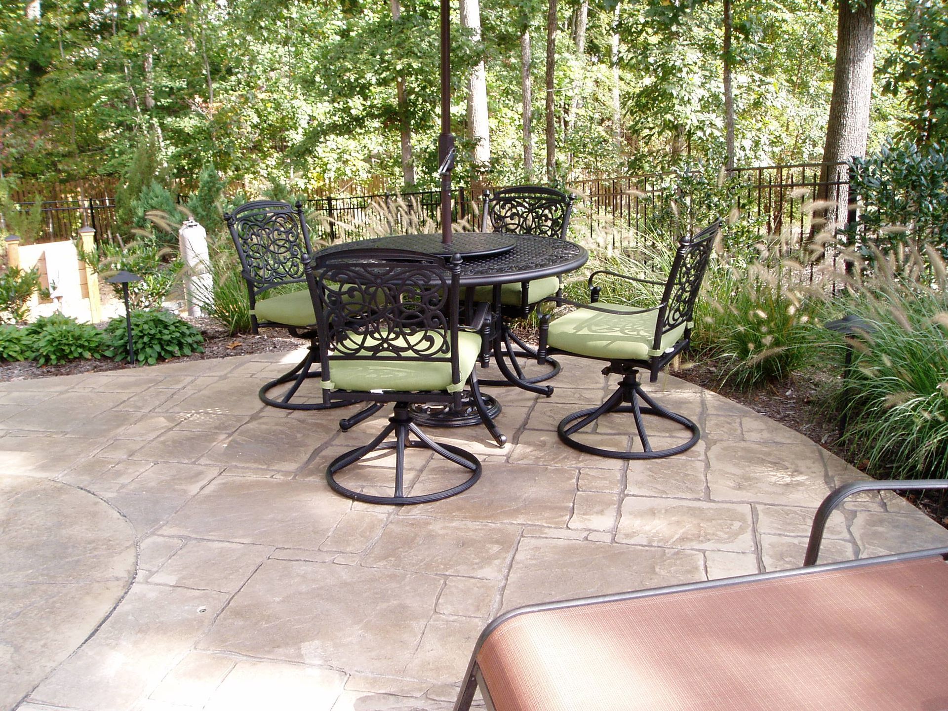 Patio with round table and four chairs with green cushions, surrounded by trees.