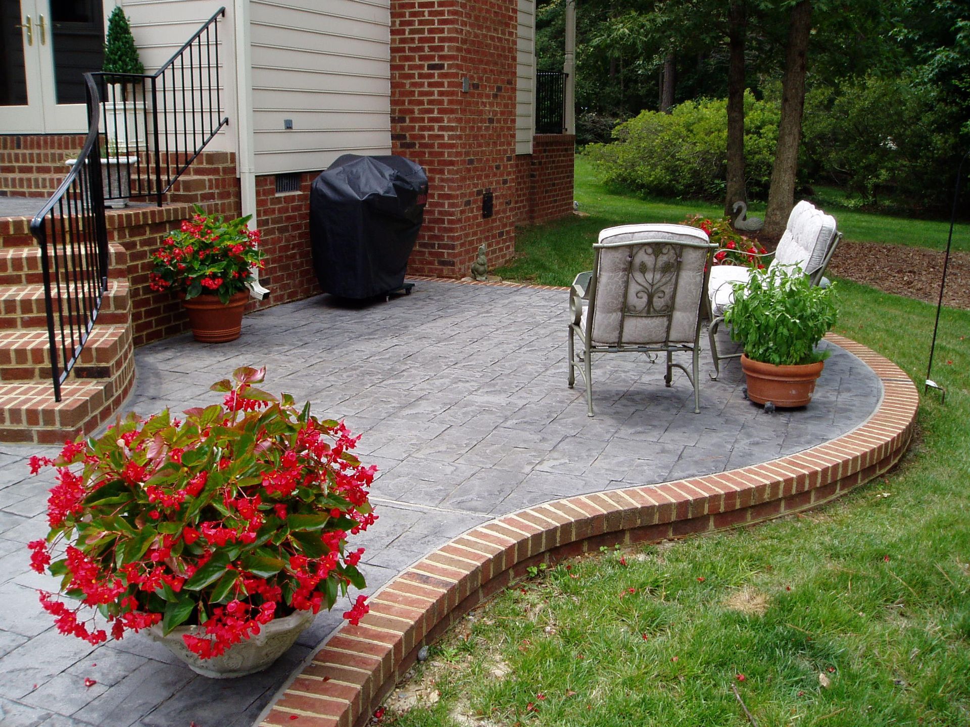 Brick patio with seating and potted flowers next to a brick house and grass.