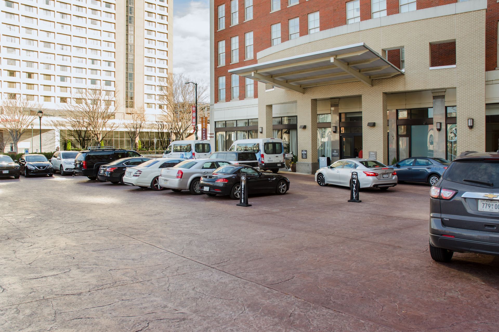 Cars parked in front of a hotel entrance. Brick facade, tall building in the background. Cloudy day.