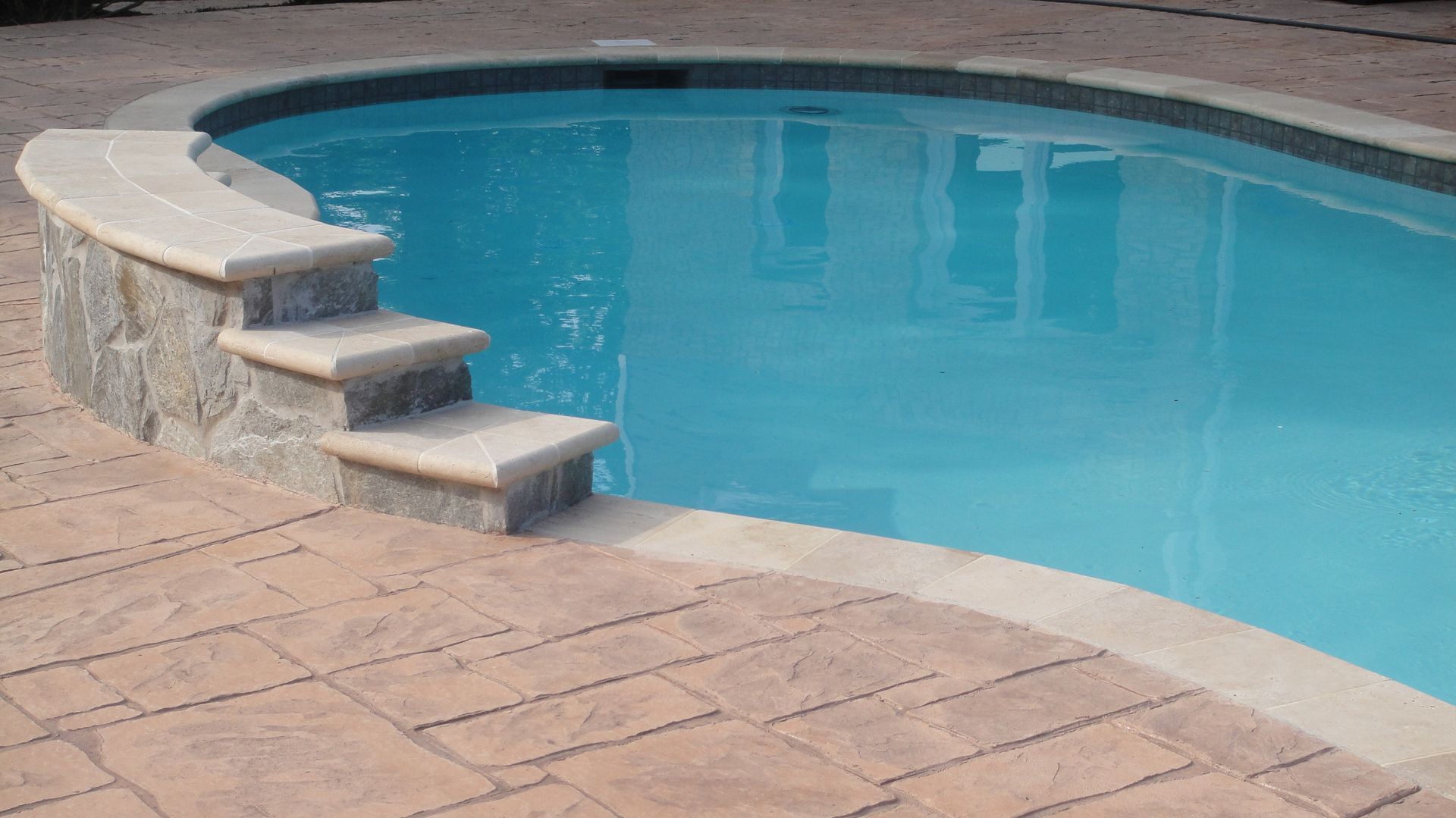 Stone steps leading into a blue swimming pool, surrounded by a stone patio.